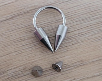 May include: A silver body piercing with two pointed ends and a circular middle section. There are two additional silver pointed ends.