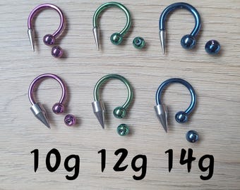May include: Three pairs of surgical steel septum rings with a pointed end. The rings are available in three sizes: 10g, 12g, and 14g. The rings are in different colors: purple, green, and blue.