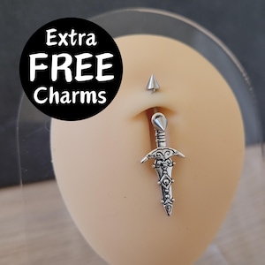 May include: A silver-colored belly button ring featuring a sword charm. The image also shows a small, silver-colored stud above the navel. A black circle with white text that reads "Extra FREE Charms" is in the upper left corner.