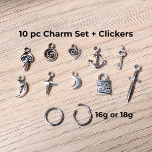 May include: A 10-piece silver-toned metal charm set and two circular clickers. The charms include a mushroom, spiral, heart, anchor, key, crescent moon with a face, four-pointed star, plain crescent moon, padlock, and sword. Text reads 10 pc Charm Set + Clickers and 16g or 18g.