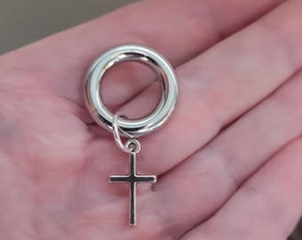 May include: A polished silver-toned circular ear gauge featuring a small, dangling cross charm attached by a thin metal jump ring. The jewelry piece has a smooth, reflective metallic finish and a hollow center, designed for stretched ear piercings.