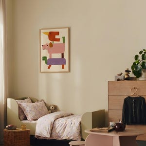Puede incluir: Un dormitorio infantil con una cama verde claro, ropa de cama floral y un estampado enmarcado de formas de animales apiladas. Una peque&ntilde;a mesa y sillas est&aacute;n en primer plano, y una c&oacute;moda con un c&aacute;rdigan colgando est&aacute; en el fondo. La habitaci&oacute;n tiene una paleta de colores neutros.