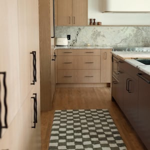 K&ouml;nnte beinhalten: Eine moderne K&uuml;che mit hellen Holzschr&auml;nken und einem karierten Teppich. Die Schr&auml;nke haben schwarze Griffe und die Arbeitsplatte eine Marmorr&uuml;ckwand. Ein wei&szlig;er Toaster steht auf der Theke. Der Teppich ist grau und wei&szlig;.