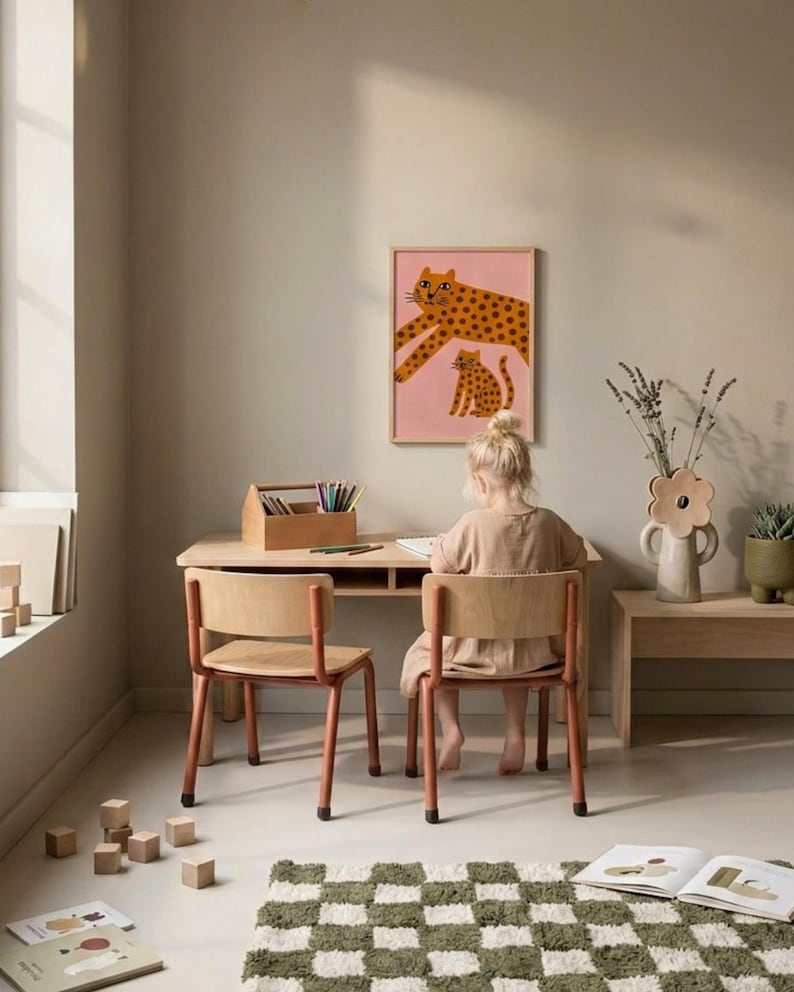 K&ouml;nnte beinhalten: Ein Kind sitzt an einem Holztisch mit zwei passenden St&uuml;hlen. Ein gerahmter rosa Druck mit einem Leopardenmuster h&auml;ngt an der Wand. Eine Holzkiste enth&auml;lt Buntstifte. Ein gr&uuml;n-wei&szlig; karierter Teppich liegt auf dem Boden.