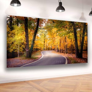 May include: A large framed canvas print of a winding road through a forest in autumn. The trees display vibrant yellow, orange, and green foliage. The road curves into the distance, inviting the viewer to explore the scenic landscape.