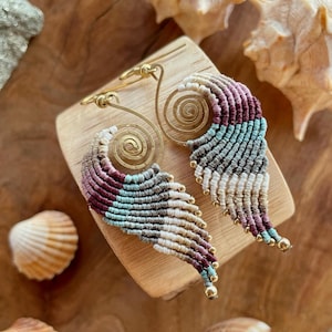 May include: A pair of long, colourful, tassel earrings with a gold spiral charm. The earrings are made of macrame and have a bohemian style.