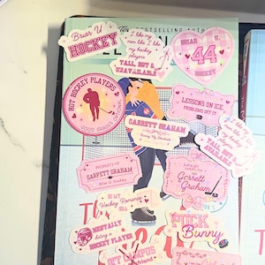 Puede incluir: Una colecci&oacute;n de pegatinas rosas y blancas con temas de hockey, que incluyen corazones, palos de hockey y texto como "Hockey Players" y "Tall, Hot & Unavailable". Las pegatinas est&aacute;n dispuestas sobre un libro.
