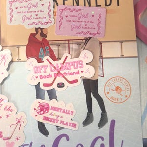 Puede incluir: Una novela titulada "The Goal" de Elle Kennedy, con pegatinas decorativas. Las pegatinas presentan frases como "Off Campus Book Boyfriend" y "Mentally doing a hockey player". La portada del libro tiene un dise&ntilde;o de pista de hockey.