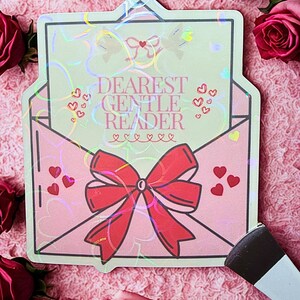 May include: A pink envelope-shaped sticker with the text "DEAREST GENTLE READER" in a script font. The sticker features a red bow, hearts, and a holographic effect. The background is a pink, textured surface with red roses.