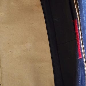 May include: Interior view of a handbag, featuring a beige fabric lining and a navy blue leather pocket with a red accent. The bag's interior shows signs of wear.