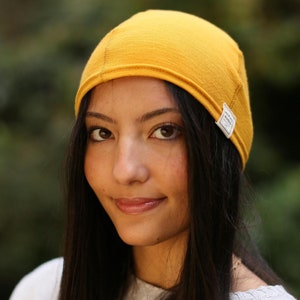 May include: A woman wearing a mustard yellow beanie with a small white label that says "Made in Canada".