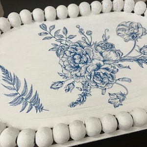 May include: White oval serving tray with a blue floral design. The tray features a beaded edge and a distressed finish. The floral pattern includes roses and other botanical elements, creating a vintage aesthetic.