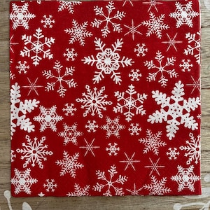 May include: A square red napkin with a repeating pattern of white snowflakes. The snowflakes vary in size and design, creating a festive winter theme. The napkin is likely made of paper and suitable for holiday gatherings.
