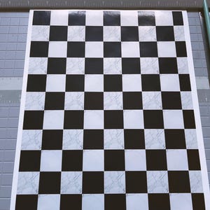 May include: A sheet of paper with a black and white checkerboard pattern. The white squares have a marble-like texture. The paper is on a gray cutting mat.