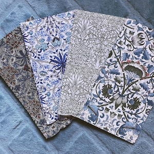May include: Four fabric pieces with floral patterns in shades of blue, gray, and brown. The designs include stylized flowers and foliage on a white background. The fabrics are arranged on a blue surface, showcasing the variety of patterns.