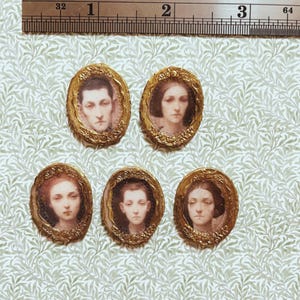 May include: Five miniature oval portraits with gold-colored frames. Each portrait features a person's face, with varying skin tones and hairstyles. The portraits are arranged on a patterned green and white surface.