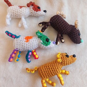 May include: Four handmade crochet dog figurines in various colors. One is white with red spots, another is brown, and two are yellow and white with colorful beaded accents. Each has black bead eyes.