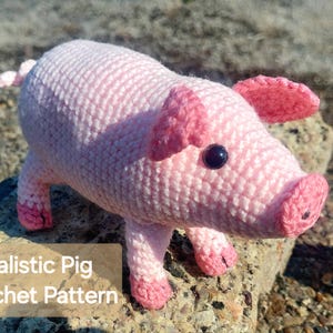 May include: A handmade, light pink crochet pig with darker pink accents on its ears, snout, and feet. The pig has a dark eye and is posed on a rock. The text "Realistic Pig Crochet Pattern" is visible.