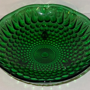 Può includere: Una ciotola di vetro verde smeraldo intenso con un motivo strutturato. La ciotola ha un bordo smerlato e un design centrale. La superficie della ciotola è ricoperta da un motivo di piccoli cerchi in rilievo.