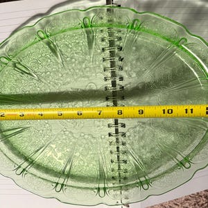 May include: A vintage green glass oval serving platter with a floral pattern. The platter is approximately 30 cm long. The edges have a scalloped design. The platter is made of a translucent green glass.