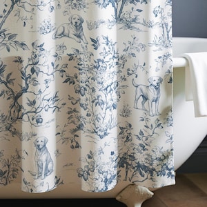 Könnte beinhalten: Blau-weißer Duschvorhang mit Toile-Muster mit Hunden und floralen Elementen. Der Vorhang hängt vor einer weißen Badewanne. Ein kleiner Holzschemel hält Handtücher und einen Seifenspender.
