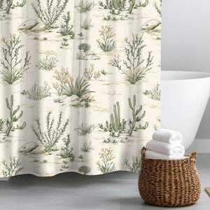 May include: A white shower curtain with a desert-themed pattern featuring cacti and other desert plants in shades of green and brown. The curtain is hanging in a bathroom with a white bathtub, a wooden side table, and a potted fern.