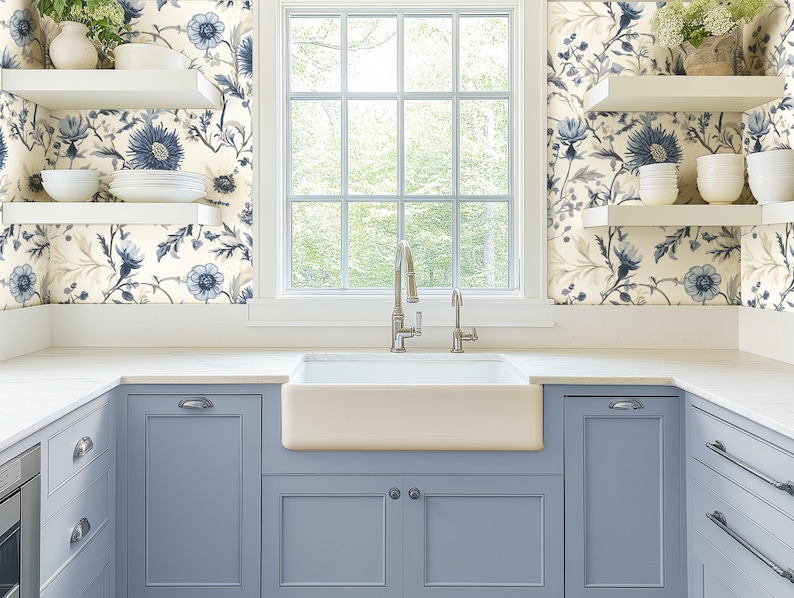 May include: A white farmhouse kitchen with blue cabinets and a white porcelain farmhouse sink. The walls are covered in a floral wallpaper with blue and white flowers.