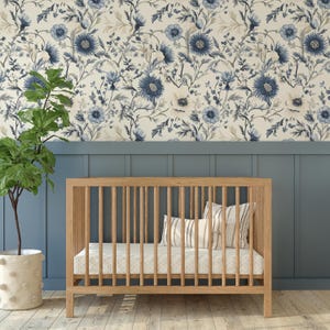 May include: A wooden cot with a white and blue floral patterned wallpaper behind it. The cot has a white mattress and a striped pillow.