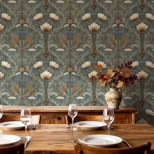 May include: A wooden dining table set with white plates and clear wine glasses, positioned in front of a wall covered in wallpaper featuring a repeating pattern of white flowers, golden wheat stalks, and green foliage, with a vase of autumn leaves.