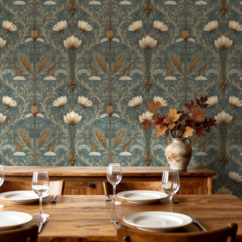 May include: A wooden dining table set with white plates and clear wine glasses, positioned in front of a wall covered in wallpaper featuring a repeating pattern of white flowers, golden wheat stalks, and green foliage, with a vase of autumn leaves.