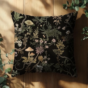 Puede incluir: Una almohada negra con estampado floral y de setas. El estampado presenta flores delicadas, hojas y setas en tonos rosa, verde y marrón.