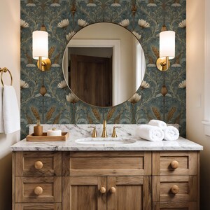 May include: A bathroom vanity with a white marble countertop, a round mirror, and two gold wall sconces. The wall features blue floral wallpaper with wheat stalks. A wooden cabinet with round knobs sits below, and white towels are stacked on the counter.