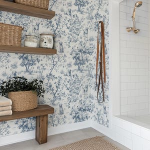 May include: A bathroom scene featuring a wooden bench with folded towels and a woven basket holding a plant. The wall has a blue and white toile wallpaper with dog and tree motifs. Woven baskets sit on wooden shelves. A leather leash hangs on the wall.