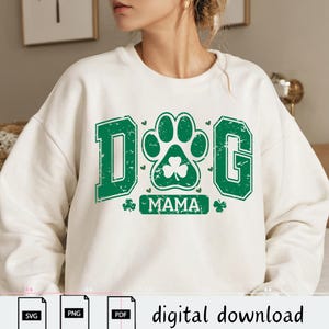 May include: White sweatshirt with a green shamrock and paw print design. The text "DOG MAMA" is printed on the sweatshirt.