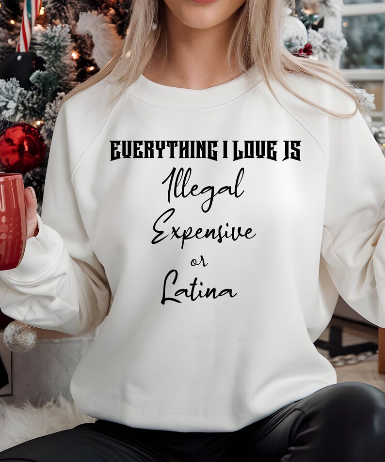 May include: White sweatshirt with black text that reads "Everything I love is Illegal Expensive or Latina".