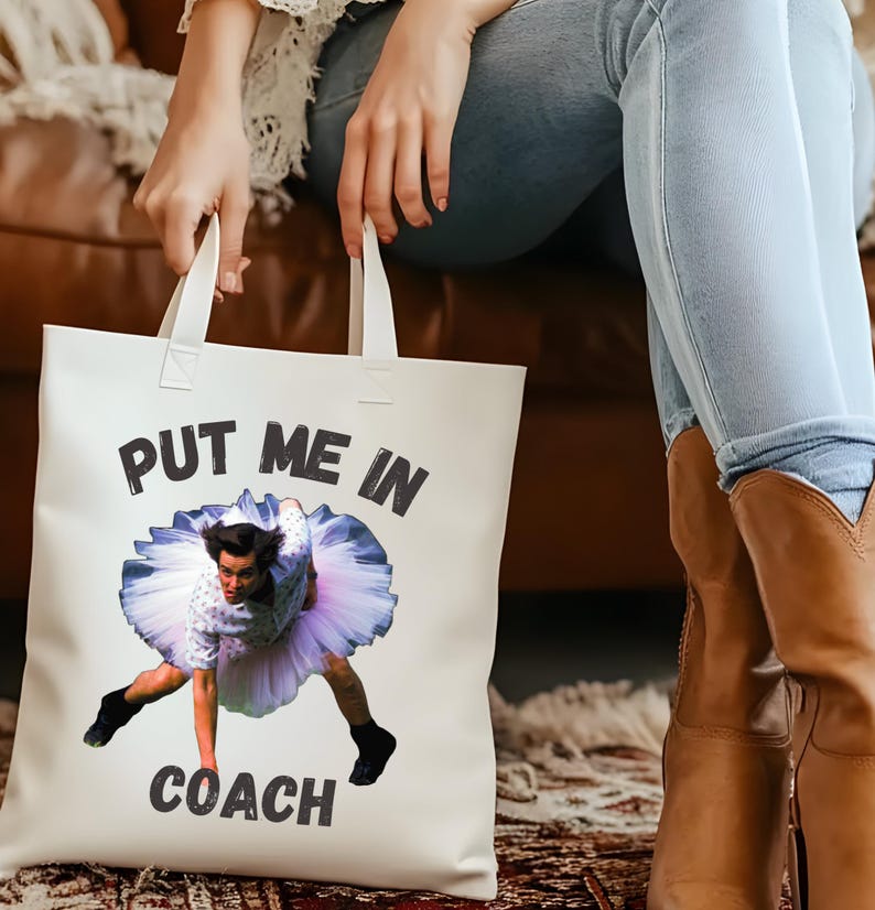 May include: White tote bag with a black and white graphic of a person in a tutu with the text "Put me in coach".