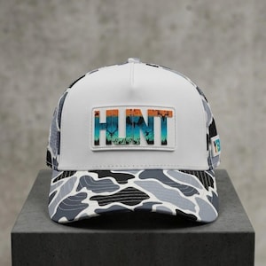 Puede incluir: Gorra de béisbol blanca y camuflaje con la palabra "HUNT" en un parche rectangular. La gorra tiene un panel frontal blanco, una visera de camuflaje y una parte trasera de malla. El texto "HUNT" está en un diseño colorido.