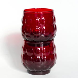 Könnte beinhalten: Zwei übereinander gestapelte rote Glasbecher mit einer Blasenstruktur.