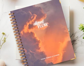 May include: A purple and orange vision journal and planner with a sunset sky background. The cover features the text "aligned FLOW" in white.