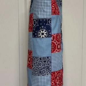 May include: A fabric bag with a Paisley Patchwork Print featuring a mix of red, navy blue, and light blue squares. The pattern alternates between traditional paisley bandana motifs and small blue and white gingham checks, hanging from a metal hook.
