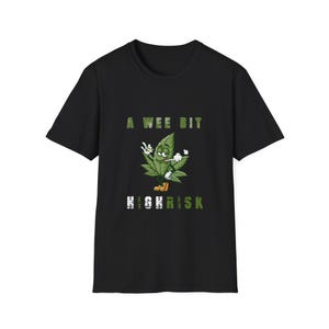 Puede incluir: Camiseta negra con una hoja de cannabis de dibujos animados fumando un cigarrillo y haciendo el signo de la paz. El texto "A Wee Bit High Risk" es en verde y blanco.