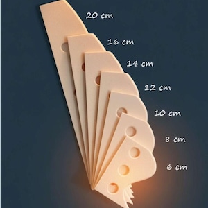 Puede incluir: Un conjunto de decoraciones de pared beige claro con forma de queso, cada una con un agujero circular y longitudes que varían de 6 cm a 20 cm. Las piezas están dispuestas en forma de abanico sobre un fondo azul oscuro.