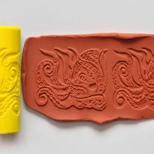 May include: A terracotta-coloured clay stamp featuring two detailed octopus designs. A yellow roller with an embossed pattern is on the left. The octopus design has tentacles and intricate details, ideal for crafting.