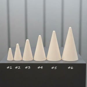 May include: Six off-white, cone-shaped objects of varying sizes are arranged in a row on a black surface. Each cone is labelled with a number from #1 to #6. The background is a light grey, vertically-lined wall.