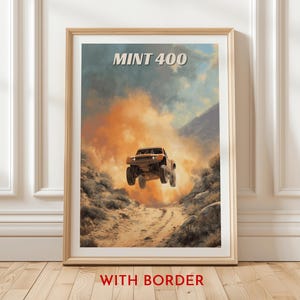 Puede incluir: Un póster enmarcado que muestra un camión todoterreno marrón en el aire sobre un camino de tierra, con el texto "MINT 400" en la parte superior. El fondo muestra un cielo polvoriento y anaranjado y montañas. Las palabras "WITH BORDER" están en la parte inferior.