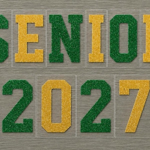 May include: Green and gold glitter letters spell "SENIOR 2027" on a gray background. The word "SENIOR" is in a block letter style, with the numbers "2027" below it. The letters and numbers are in individual clear squares.