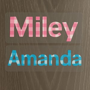 May include: Two rectangular name decals. The top decal reads "Miley" in pink and white gingham print. The bottom decal reads "Amanda" in blue and white gingham print. Both decals are on a clear background.