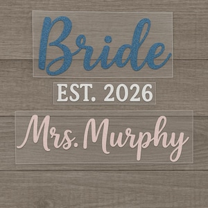 May include: Three clear acrylic rectangles with text. The top rectangle has the word "Bride" in blue glitter. The middle rectangle reads "EST. 2026" in white. The bottom rectangle says "Mrs. Murphy" in pink glitter.