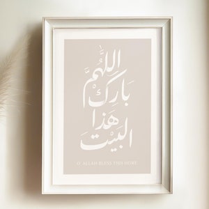 Puede incluir: Una impresión enmarcada con un fondo beige y caligrafía árabe blanca. El texto se traduce como "Oh Allah bendice este hogar". La impresión está en un marco blanco y tiene la palabra "tabarak" en la esquina inferior derecha.