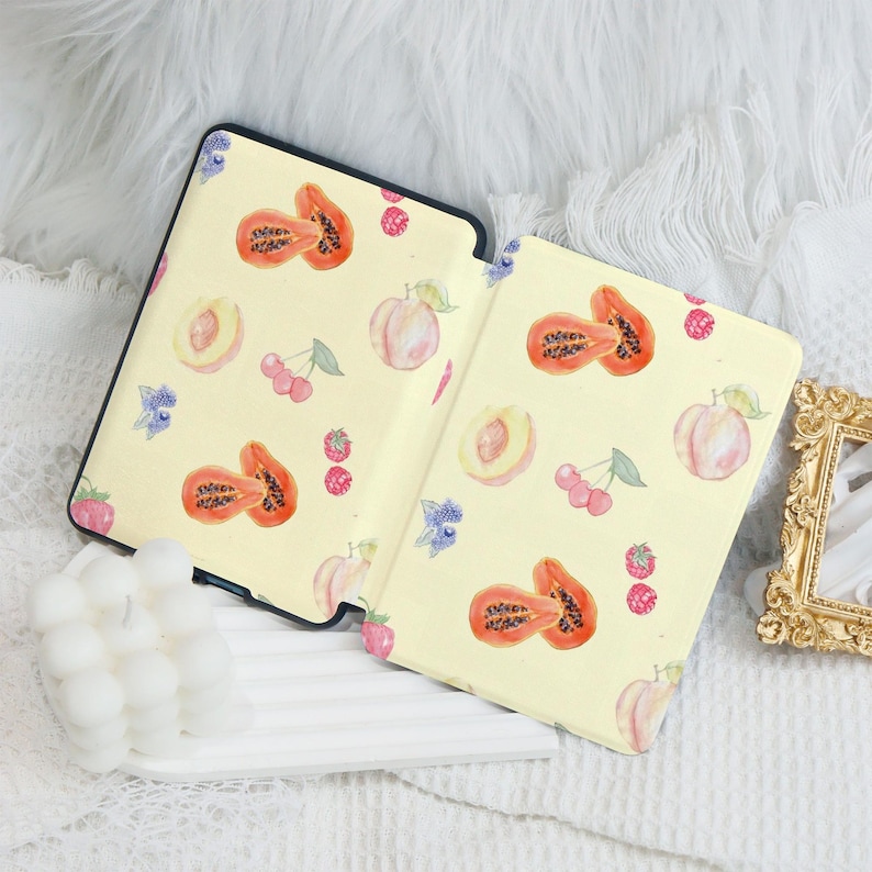 May include: A yellow e-reader cover with a watercolor design of papaya, peaches, and cherries. The cover is open and the e-reader is visible.